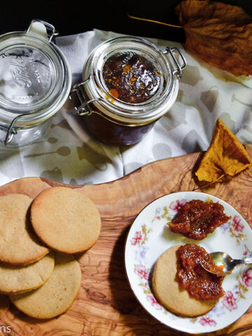teaspoon spreading pumpkin jam on a chestnut cookie next to more cookies