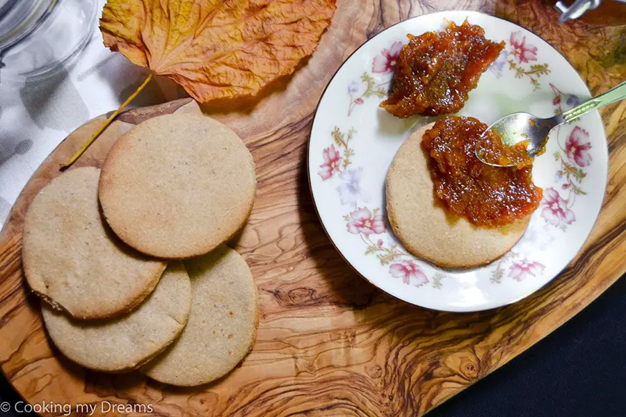 teaspoon spreading pumpkin jam on a chestnut cookie next to more cookies
