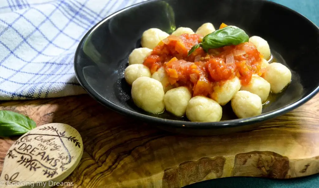 Black plate with gnocchi and tomato sauce on top.