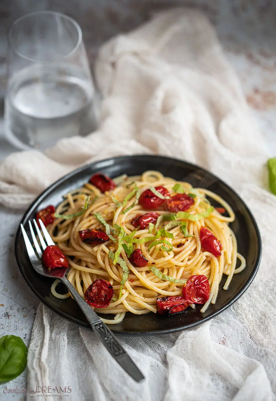 black plate with spaghetti and roasted cherry tomatoes