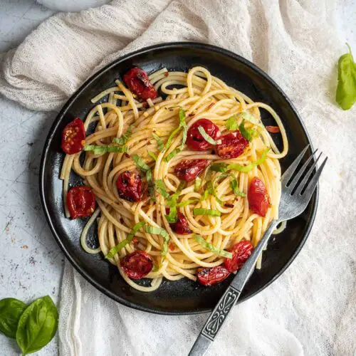 black plate with spaghetti and roasted cherry tomatoes