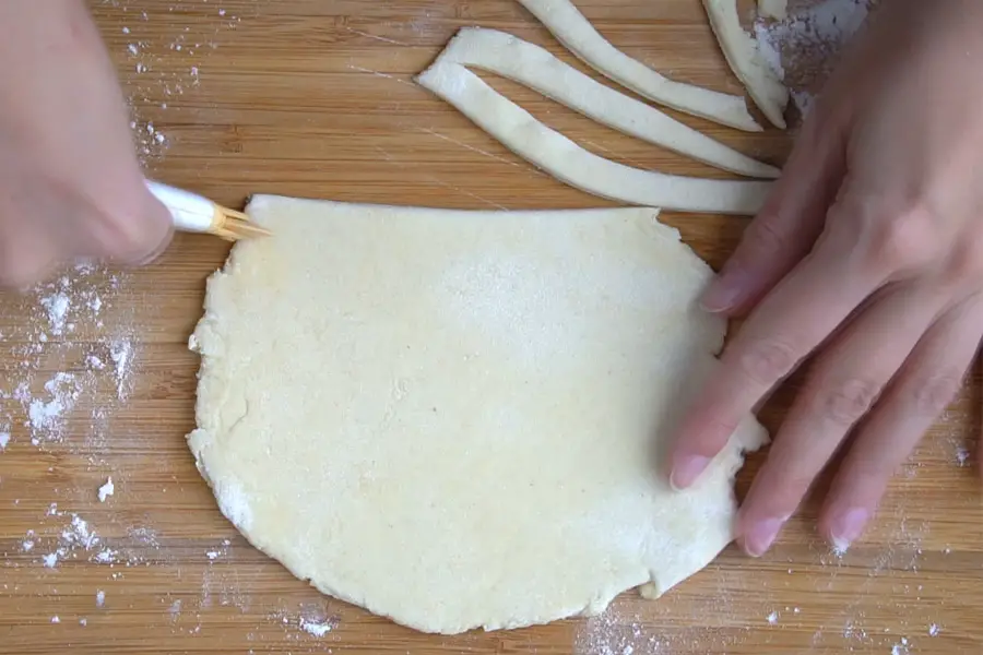 hand cutting strips of pasta dough on a wooden board