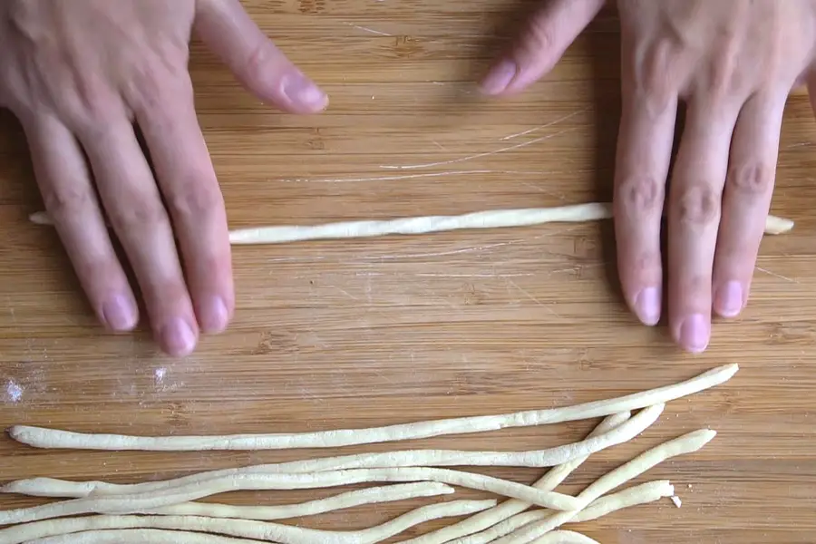 hands rolling the pici pasta on a wooden board