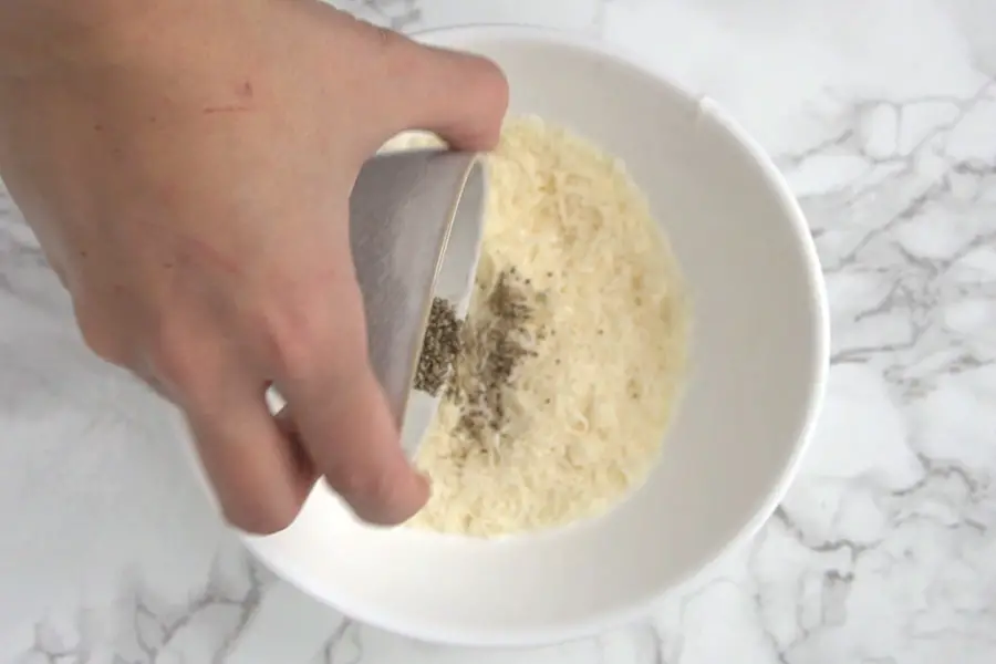 hand adding ground pepper to a bowl with romano cheese