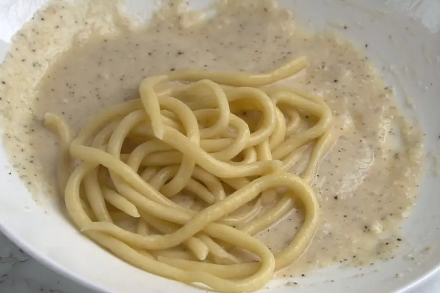boiled pasta is added to a bowl with cacio e pepe sauce