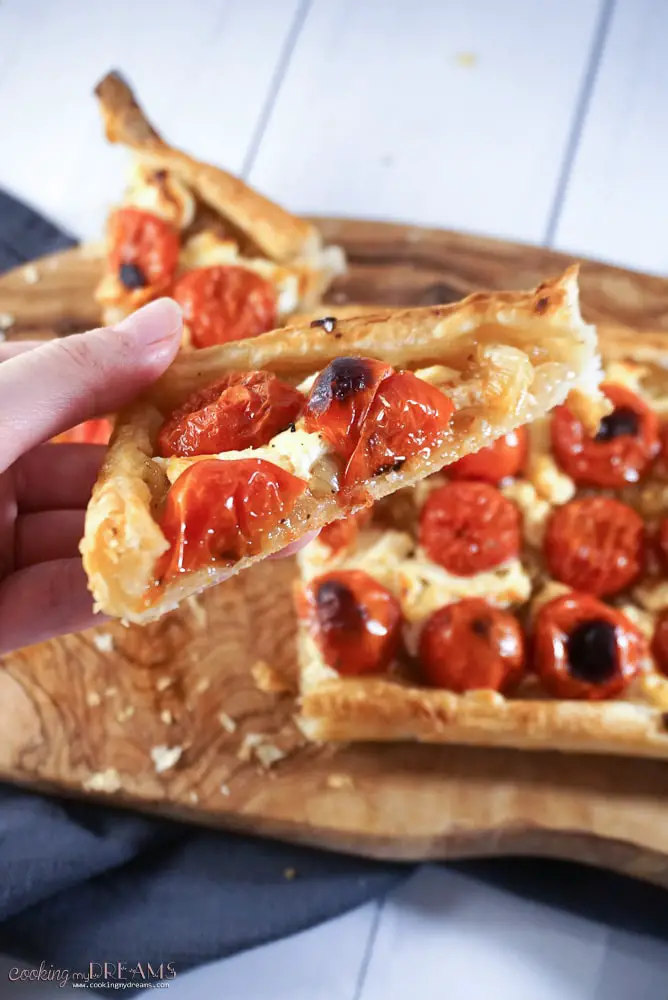 hand holding a slice of goat cheese tomato tart