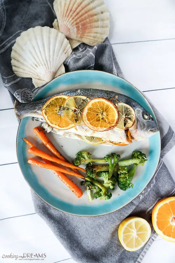 Overhead photo of cooked sea bream with citrus slices and a side of vegetables
