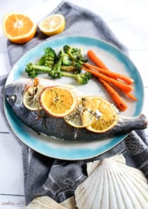 Overhead photo of cooked sea bream with citrus slices and a side of vegetables