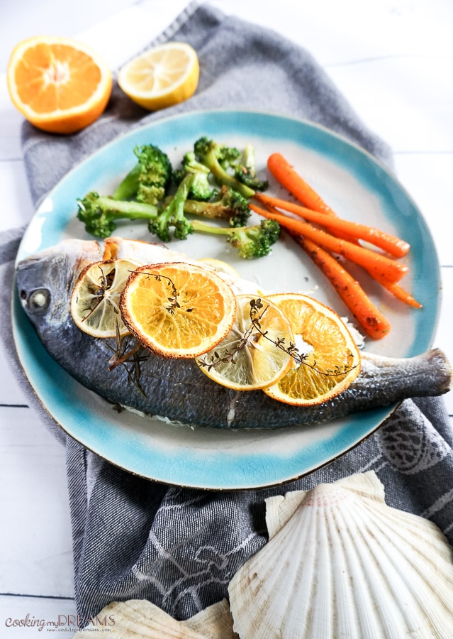 Overhead photo of cooked fish with citrus slices and a side of vegetables