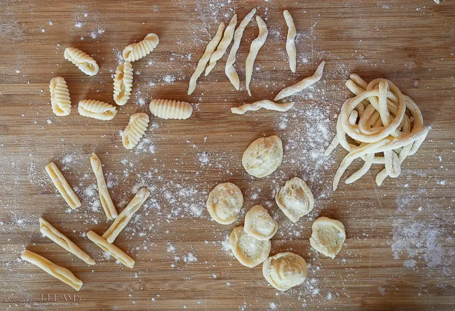 5 different raw pasta shapes on a cutting board dusted in flour
