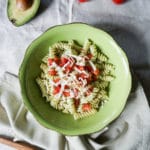 green plate with fusilli pasta, avocado sauce and cherry tomatoes