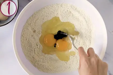 hand mixing eggs, flour, and squid ink in a bowl with a fork.