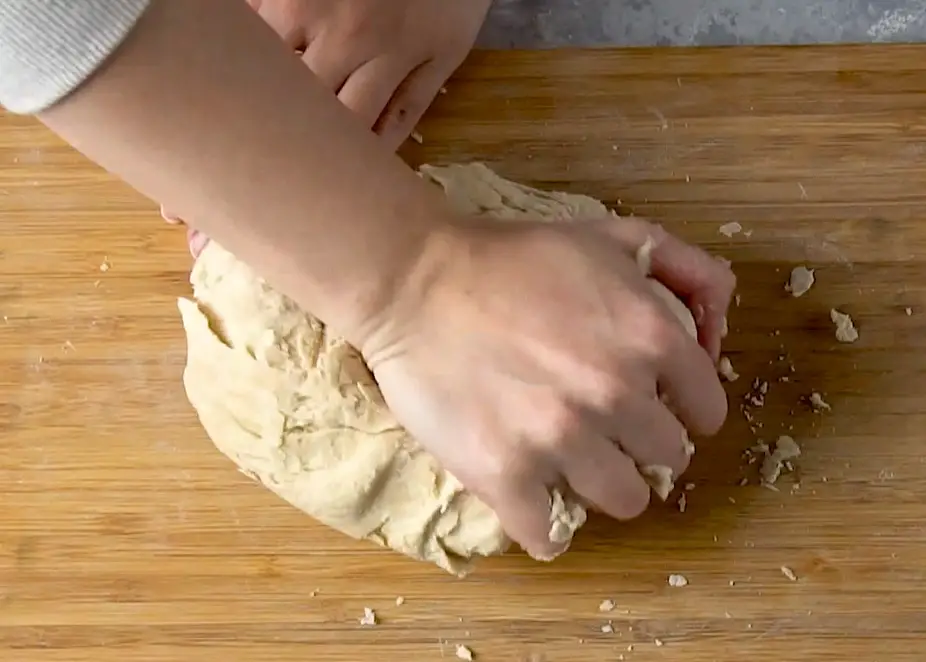 hands kneading focaccia dough on a wooden board