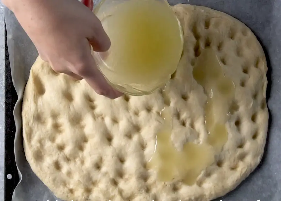 hand pouring oil on the focaccia bread before baking