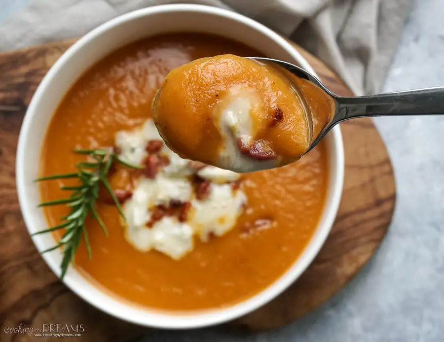 Spoon and bowl with creamy sweet potato soup topped with bacon and gorgonzola