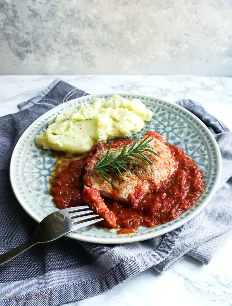 plate with pork chop in tomato sauce and mashed potatoes