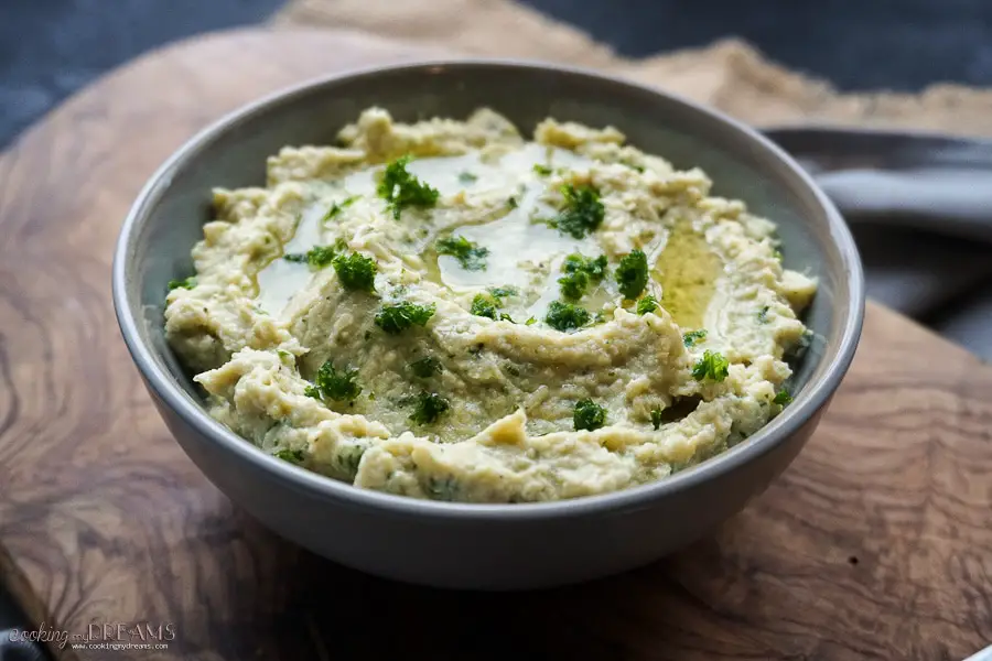 close up of a bowl of artichoke dip with olive oil and parsley on top