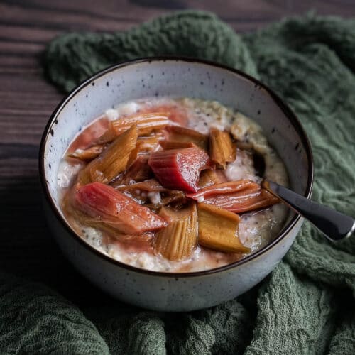 vanilla oatmeal in a bowl topped with roasted rhubarb and a spoon
