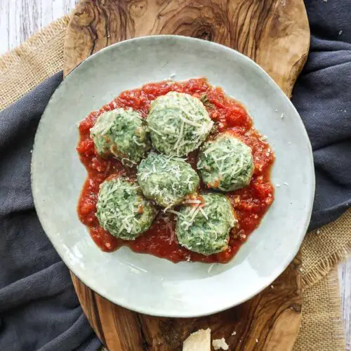 plate on a wooden board with tomato sauce and spinach and ricotta gnocchi