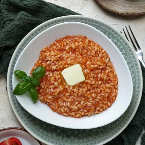 overhead of tomato risotto in a white plate with basil leaves