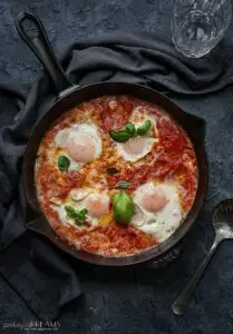 overhead of skillet with tomato sauce, eggs and basil