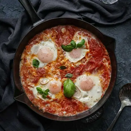 overhead of skillet with tomato sauce, eggs and basil