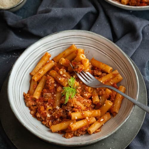 white dish with pasta with sausage tomato sauce with a fork