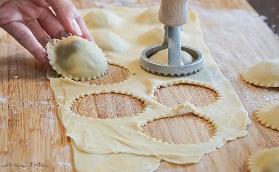 hand holding a raw ravioli on a wooden board