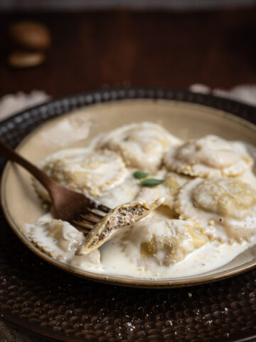 fork holding half mushroom ravioli on a plate