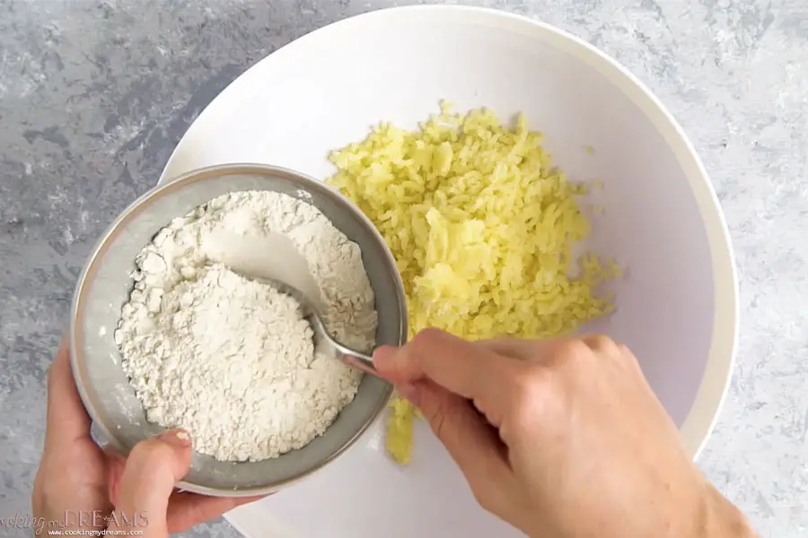hands adding flour to a bowl with riced potatoes