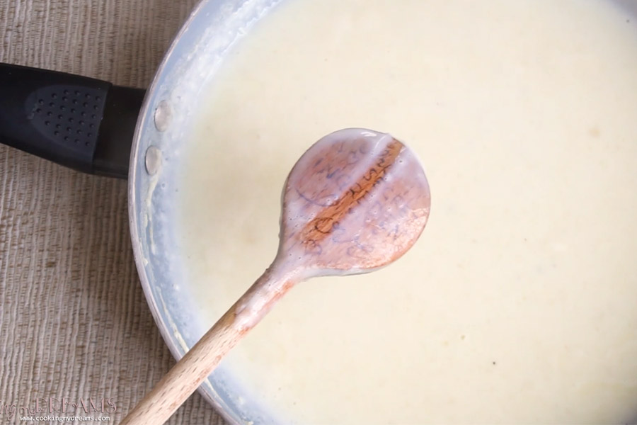 wooden spoon mixing bechamel sauce in a pan