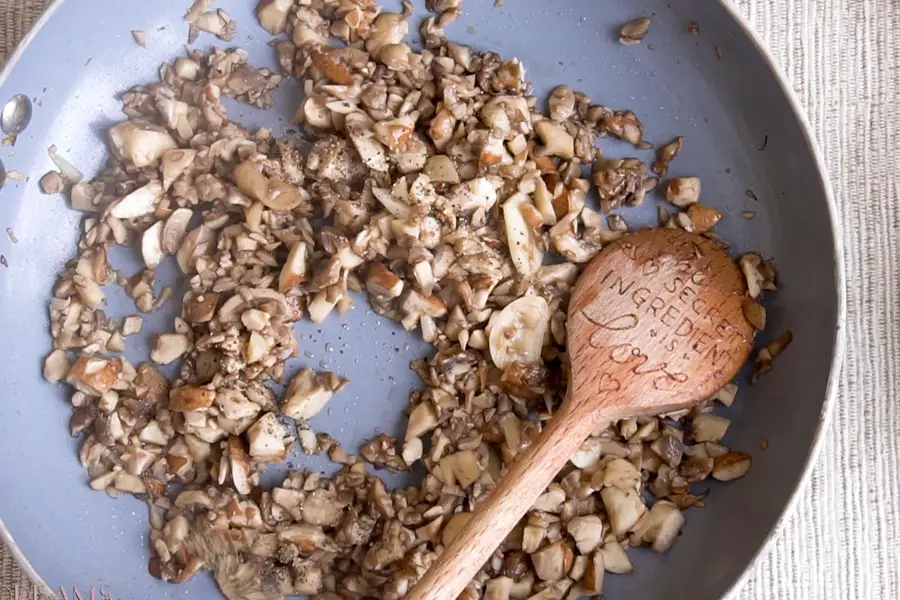 wooden spoon mixing minced mushrooms in a pan