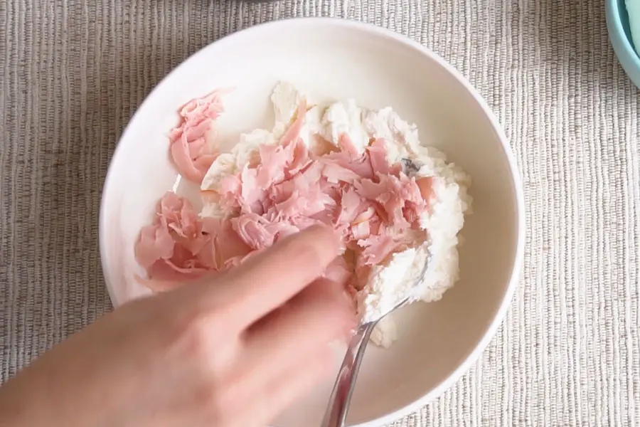 hand adding shredded ham to a bowl with ricotta