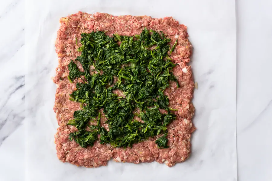 cooked spinach are spread on top of the ground beef square