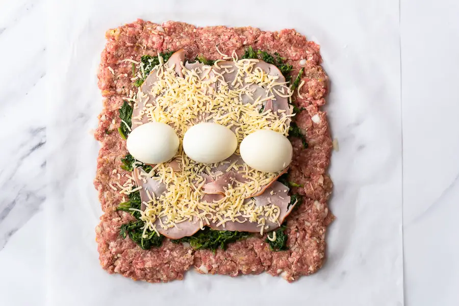 grated cheese and boiled eggs are added in the center of the meatloaf square