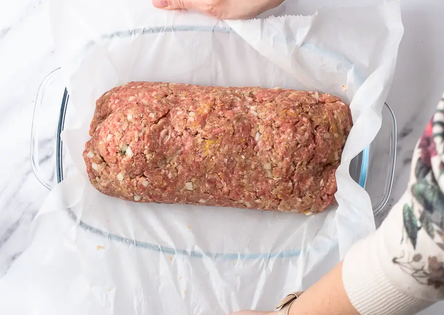 stuffed meatloaf roll is added in a baking dish with the parchment paper