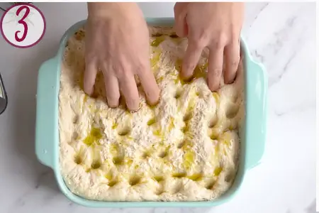 hands pushing holes into the focaccia in a baking dish