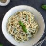 plate with creamy spaghetti with zucchini and basil leaves on top