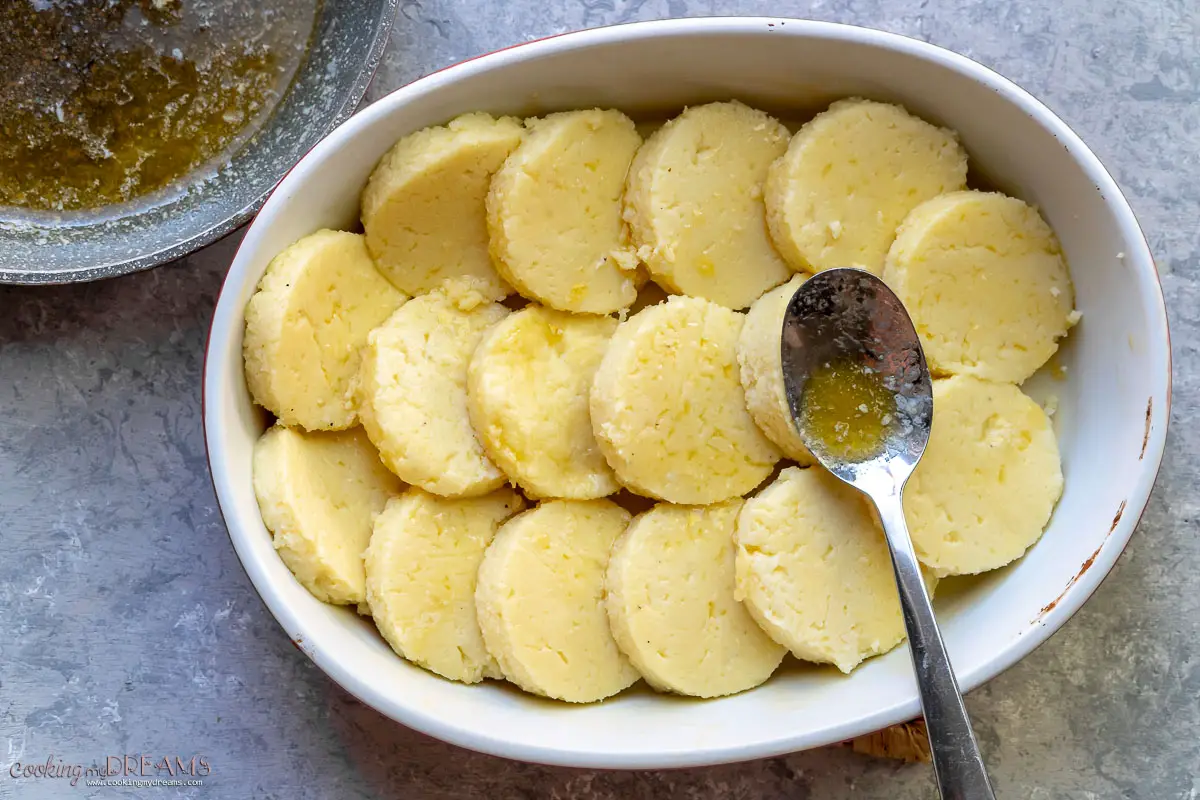 semolina gnocchi placed in an oval baking dish with a spoon