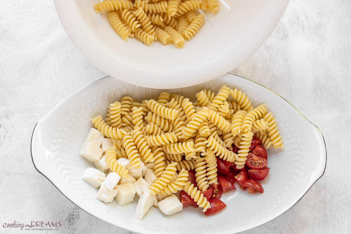 pasta being added to a bowl with tomatoes and mozzarella.