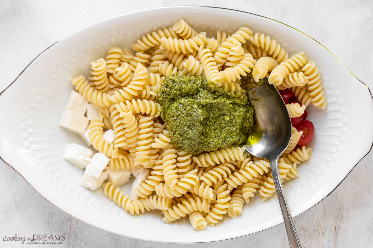 bowl with pasta, and a spoon with basil pesto on top.