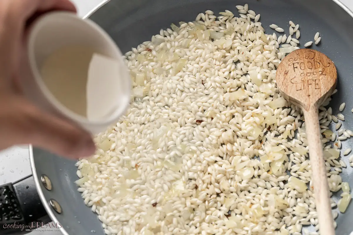 hand adding wine to the risotto in a pan