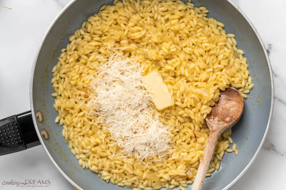 butter and parmigiano are added to the risotto in the pan with a wooden spoon
