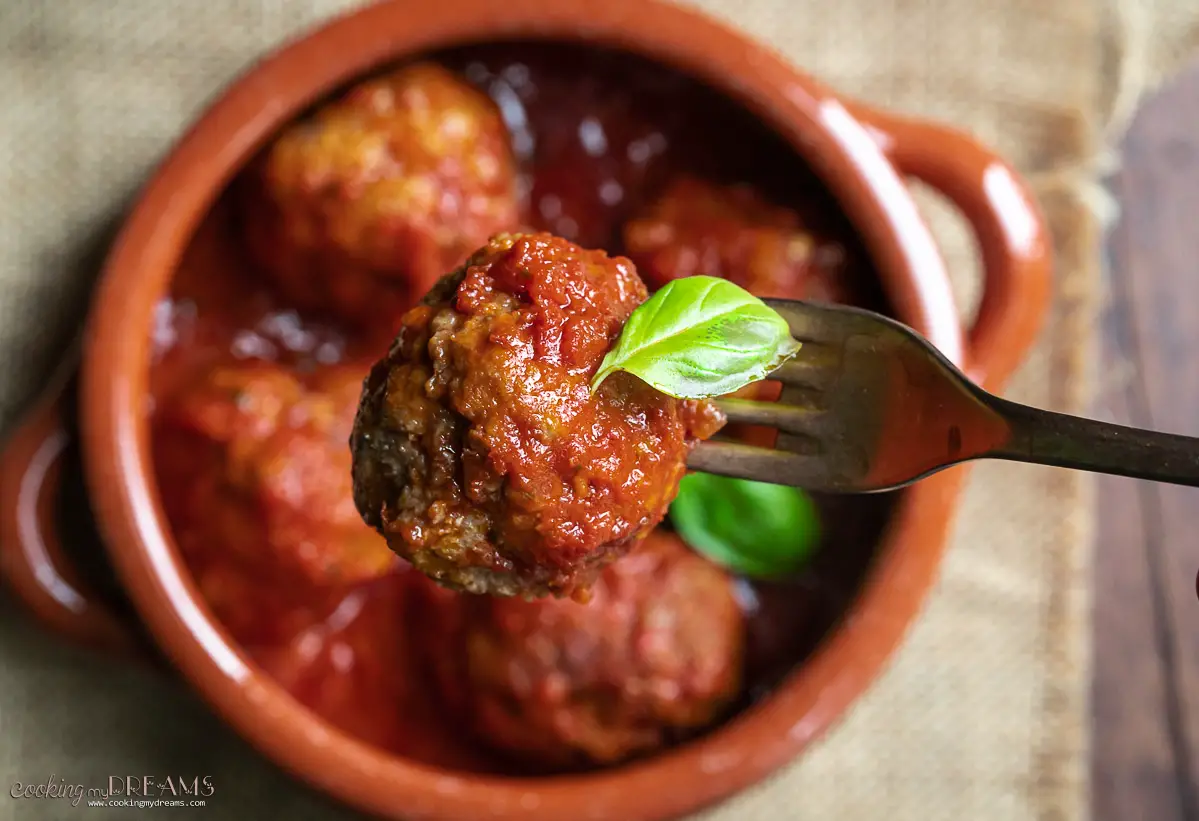 fork holding a meatball in tomato sauce with a basil leaf
