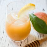 glass with peach and honey lemonade next to a peach