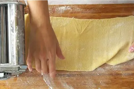 hands rolling out a pasta sheet with a pasta machine