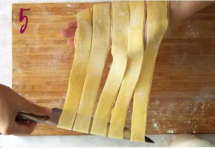 hands unrolling pasta strips into pappardelle on a wooden board