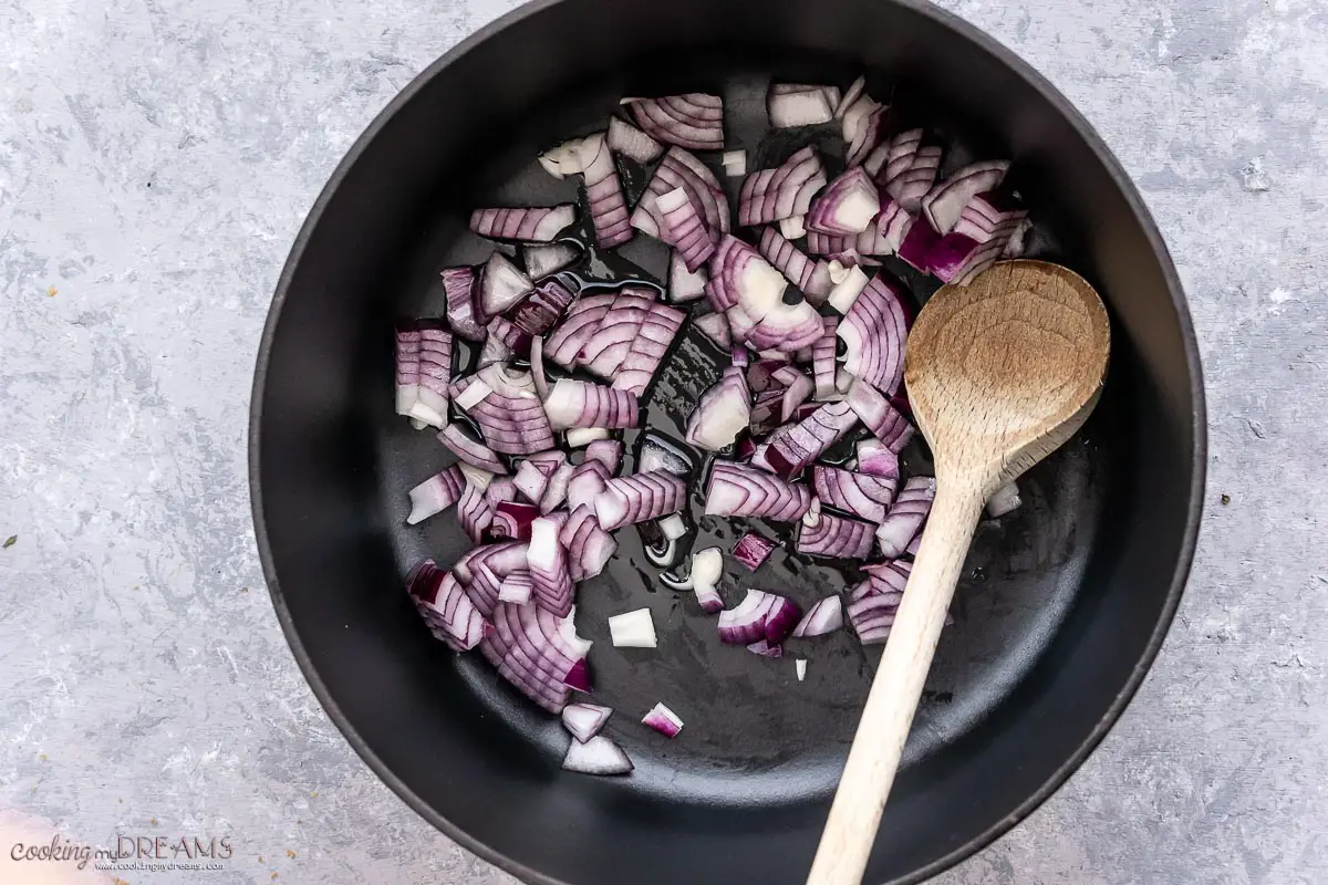onions frying in a skillet with a wooden spoon