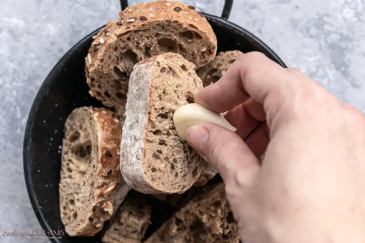 hand rubbing a garlic clove on bread slices