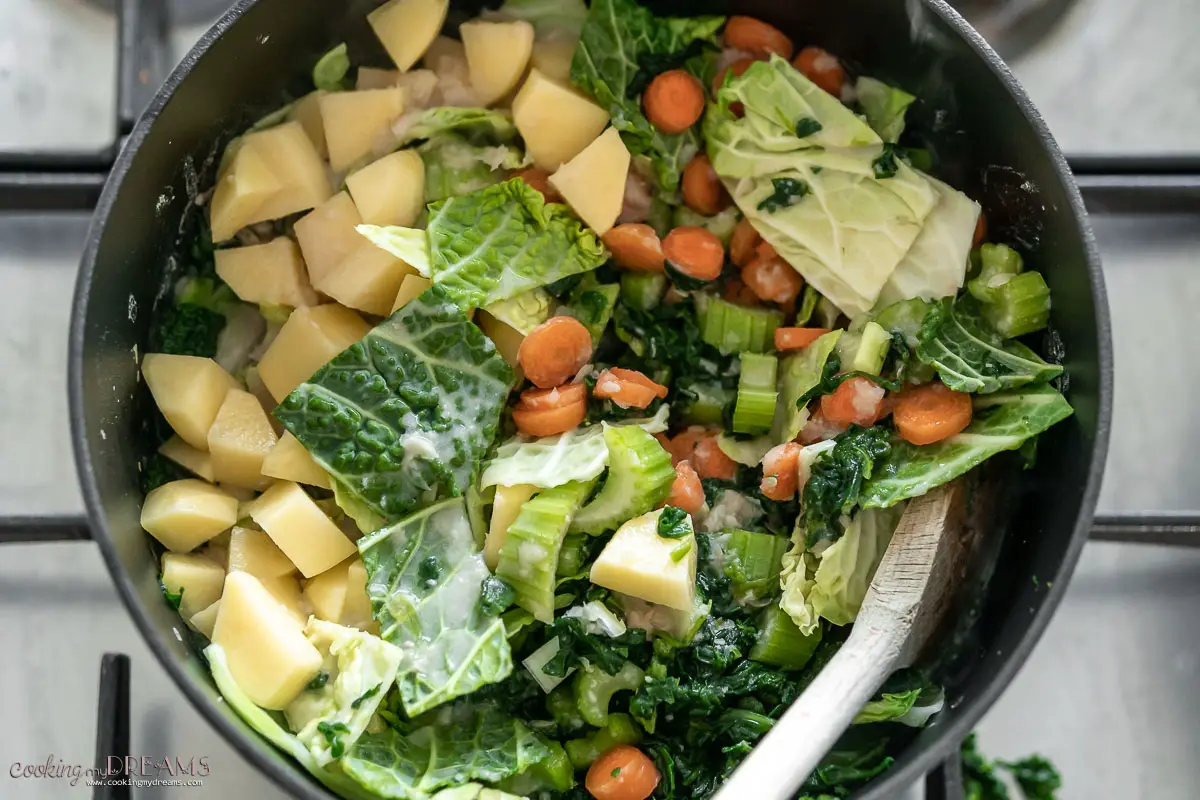vegetables and potatoes added in a large pot with a wooden spoon